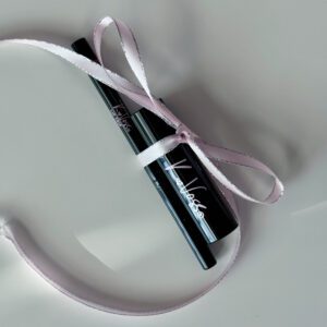 A black lipstick tube tied with a pink ribbon on a white surface.